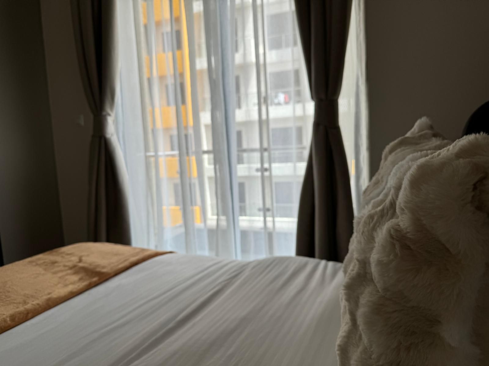 Bedroom with white linen and a soft throw, looking out through sheer curtains to the balcony